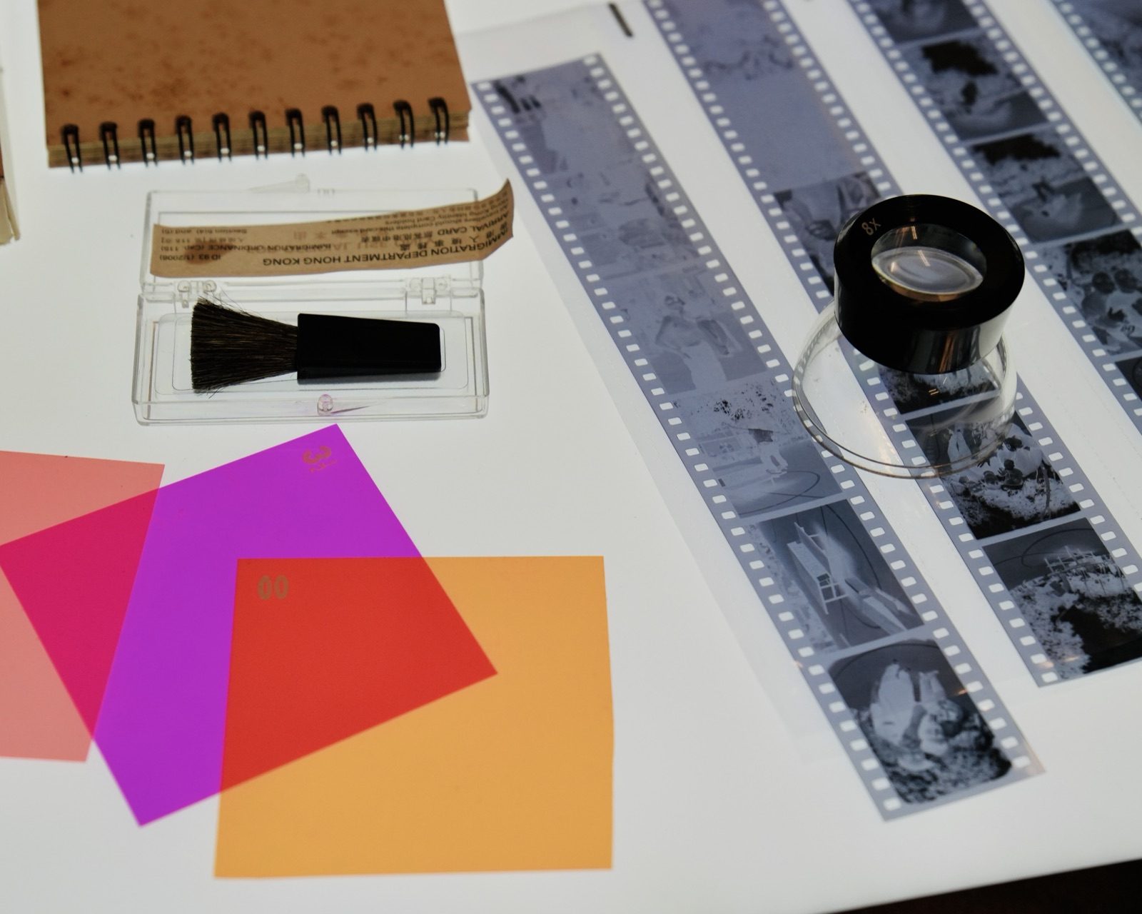 Tiras de negativos, una lupa y filtros de color sobre la mesa de luz del darkroom
