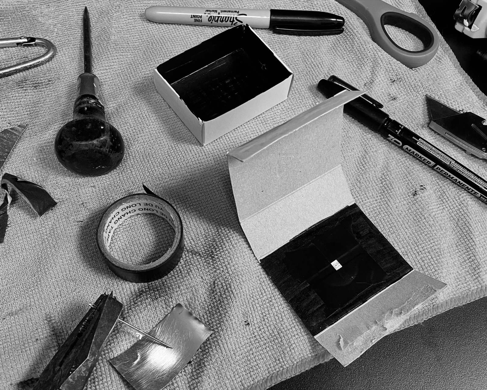 Mesa de trabajo del taller pinhole: cajas, cinta y herramientas para construir la cámara estenopeica